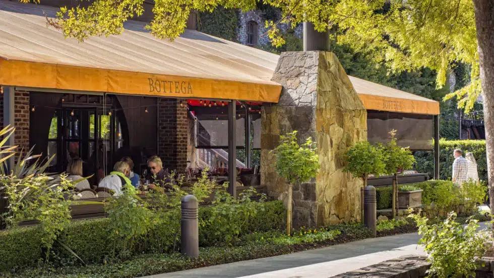The shaded terrace at Bottega Napa Valley in Yountville, set for dinner service beneath the awnings