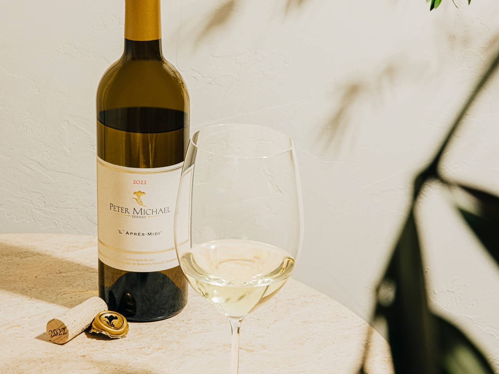A bottle of Peter Michael 2022 L'Après-Midi Sauvignon Blanc beside a poured glass