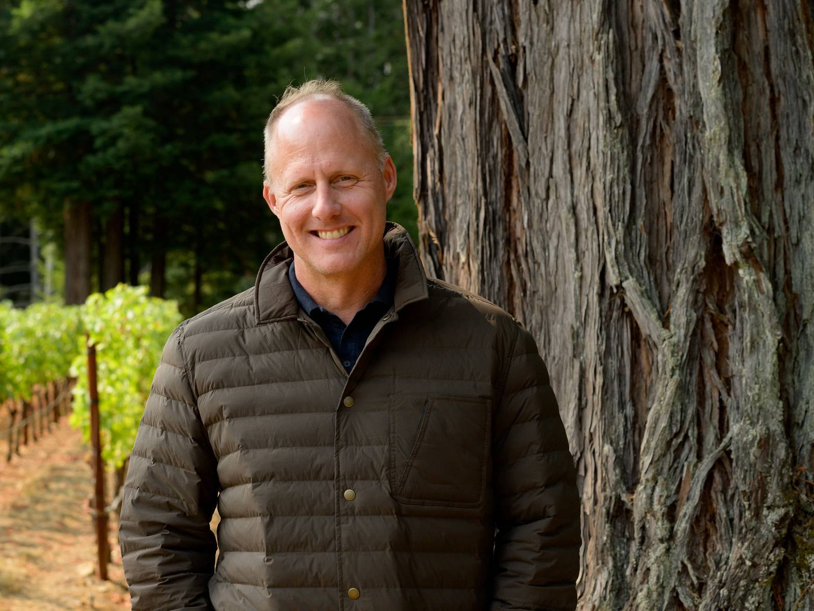 Winemaker Thomas Rivers Brown standing in a vineyard beside a redwood tree