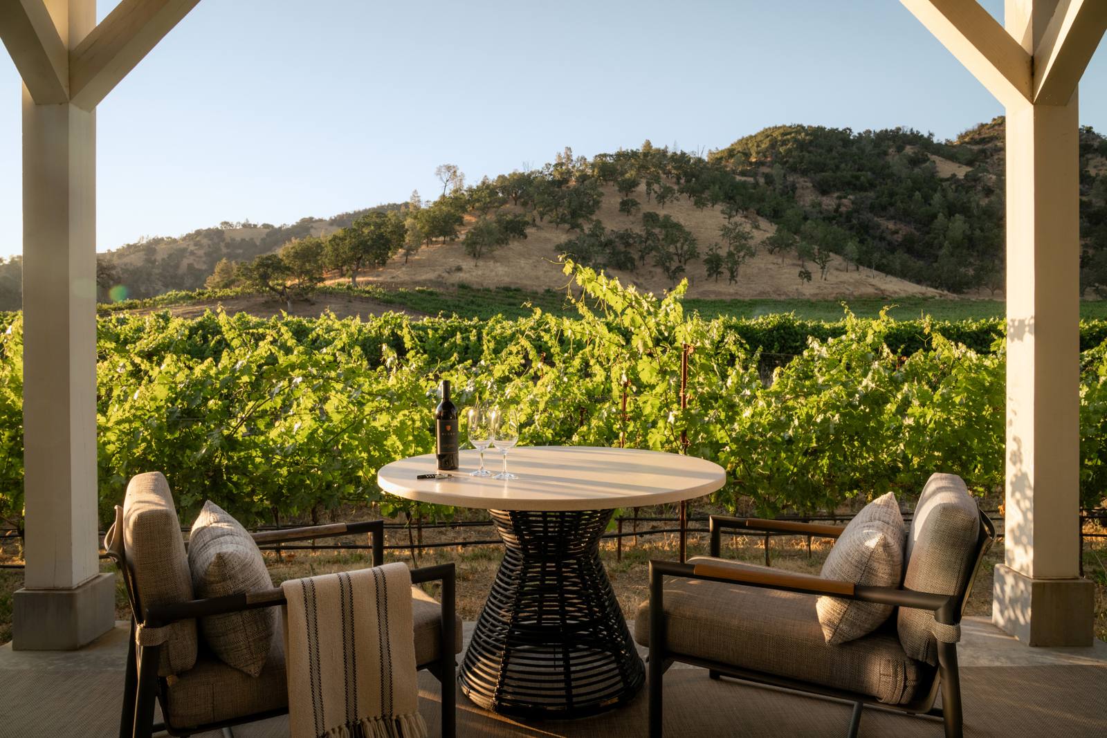 A private terrace at Four Seasons Resort and Residences Napa Valley, with a bottle and two glasses overlooking the estate vineyard