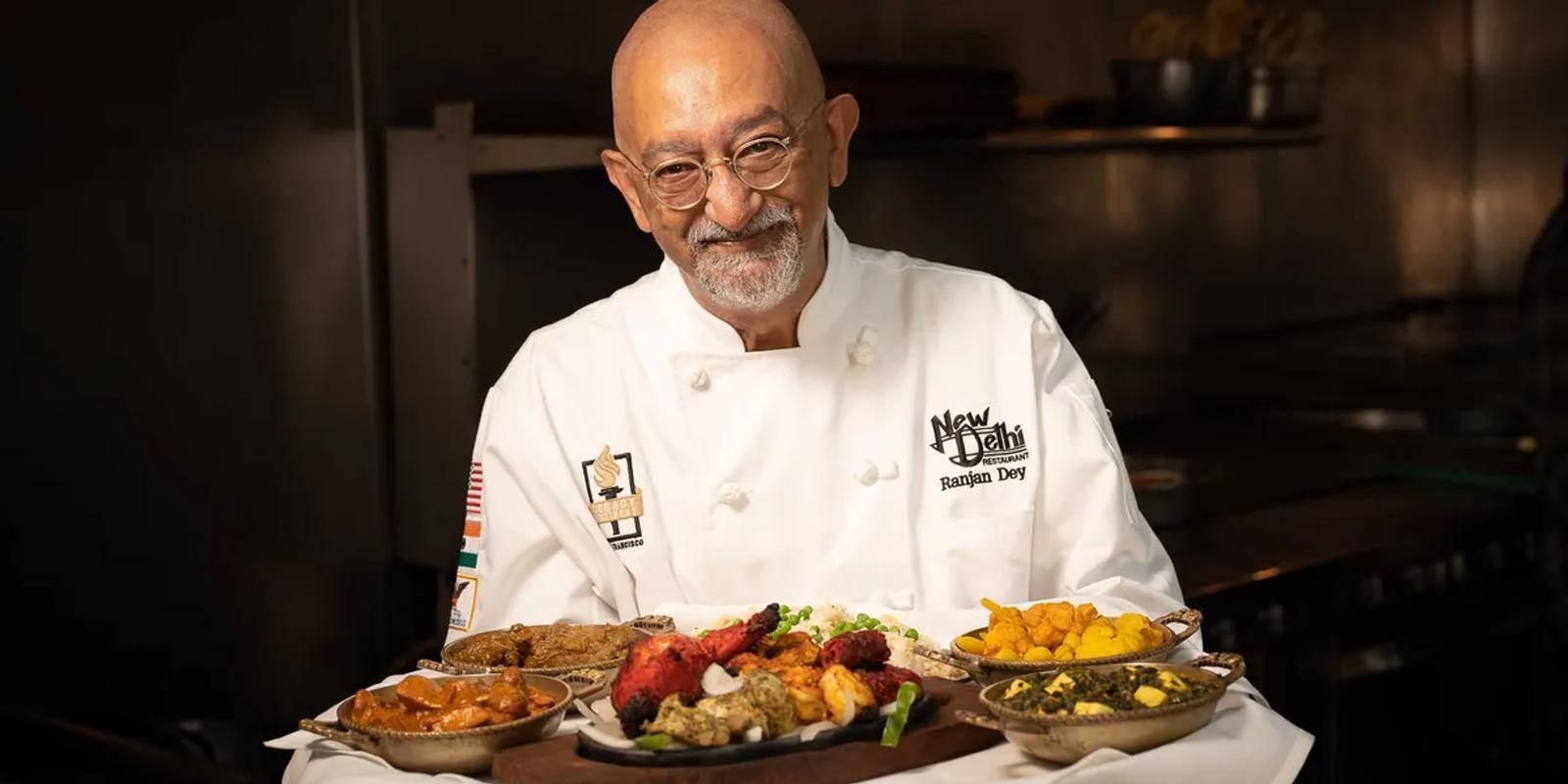 Chef Ranjan Dey in his chef whites, holding a tray of Indian dishes at Rotation Napa