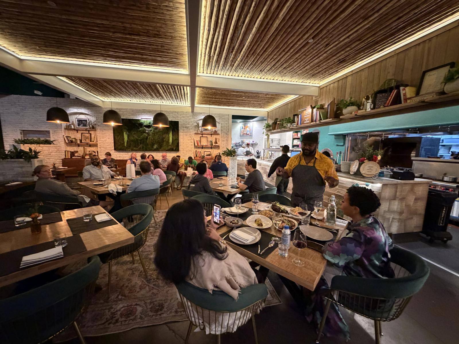 The dining room at Rotation Napa, with guests at wooden tables and the open kitchen beyond