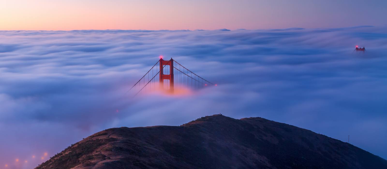 The Golden Gate Bridge rising above fog at sunrise